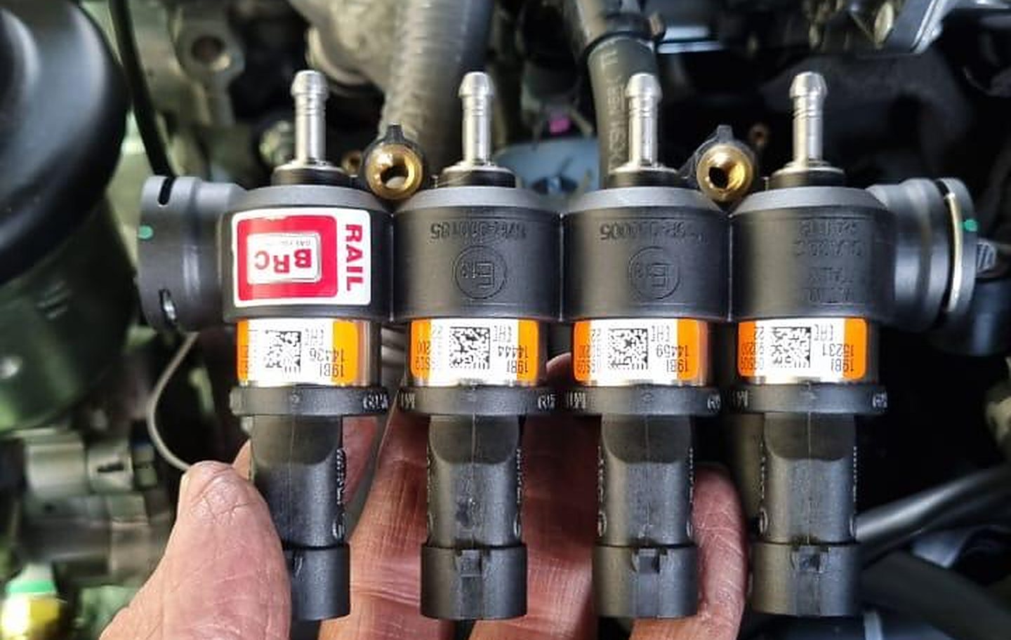 BRC gas injector rail held above a car's engine